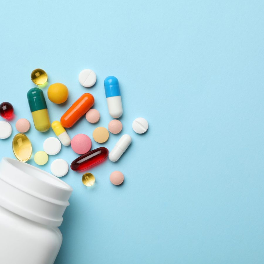 Bottle and scattered pills on color background, top view. Space for text